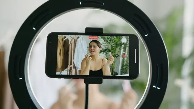 A beauty vlogger applying lipstick in a vlog recording using a smartphone and ring light. What agency reviews for beauty influencers should cover