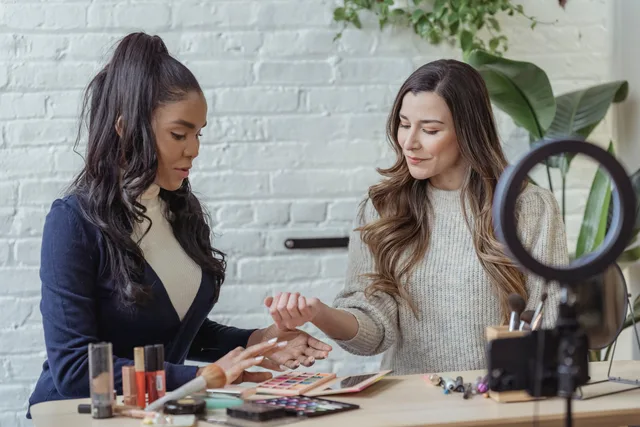 Young positive multiethnic female bloggers testing makeup products while sitting at table and recording vlog on smartphone placed on tripod with ring light. Five fields every beauty creator partnerships planning template needs