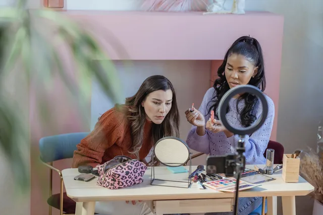 Diverse focused friends at table with eyeshadows and cosmetics near ring lamp in fashion studio. Before you sign a beauty influencers service standards agreement
