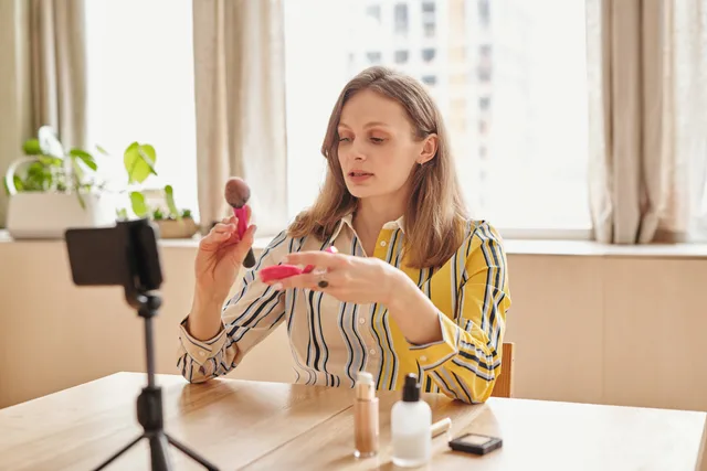A woman demonstrating makeup techniques for a vlog using cosmetics at home. Which beauty creator partnerships team roles do you need in England?